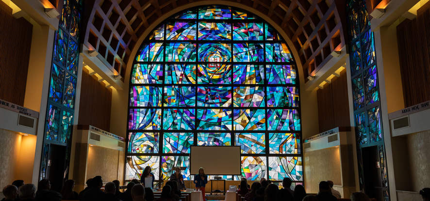 Students and parents are gathered in Stauffer chapel, looking at the front, of the reflection from the stained glass