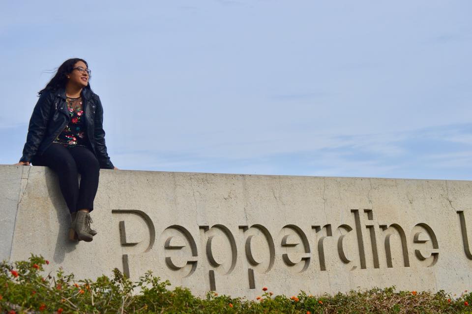 Seaver student sitting atop the Pepperdine University sign in Malibu