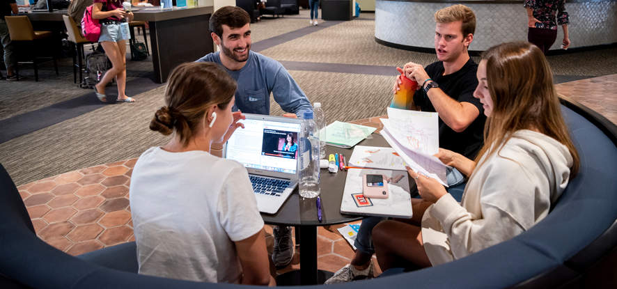 Seaver students sitting together at a round table, with a laptop and notes on it, at the Payson Library