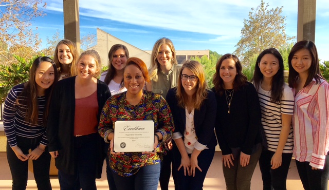 Smiling Students and Professors Gather around a certificate, the award.