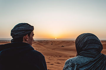 two people in the desert at sunset with headwraps 
