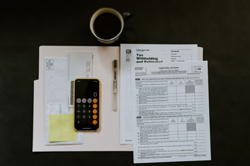 A calculator, tax file, and coffee mug against a dark background