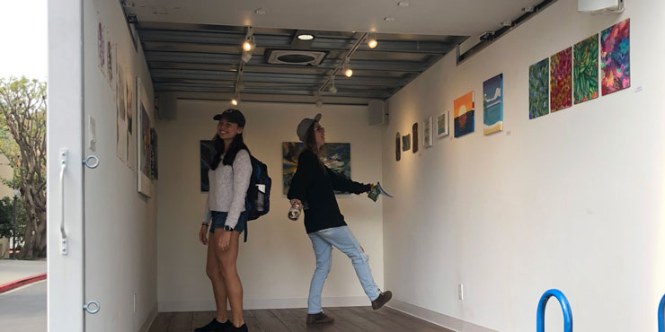 Two female students admiring artwork on the walls inside Pepperdine's mobile art gallery