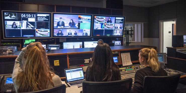 Back of Seaver students pictured in the NewsWaves control room, looking at multiple screens