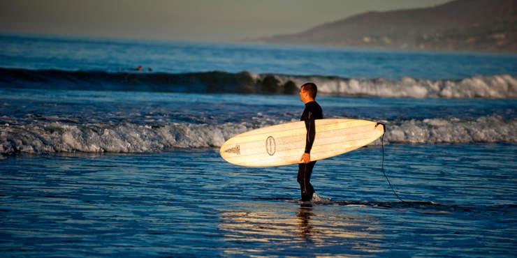 Seaver student holding a surfboard, standing in the ocean