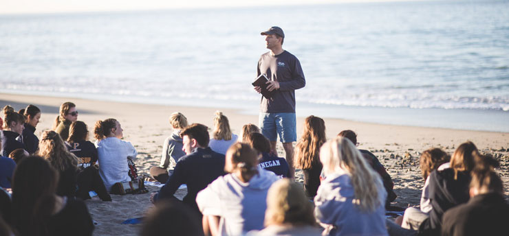 Pastor holding a sermon on the beach to a crowd of students attending surf convocation