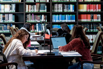 Two students studying at a desk in Payson library. One is working on a laptop and the other is taking notes. 