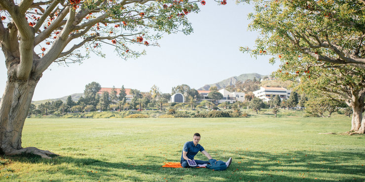 Male student sitting on an orange blanket on alumni park, unpacking books to study