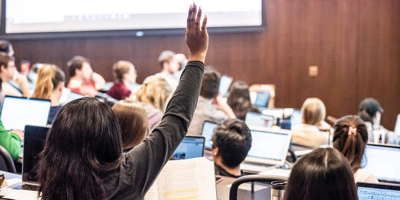 Female student raising her hand in a classroom filled with students