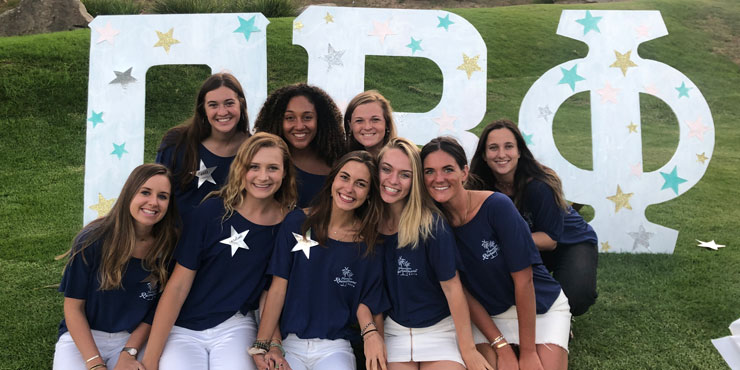 Lanie Jones seated on the grass surrounded by her sorority sisters with their Greek letters behind them