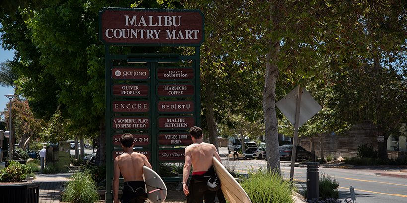 Surfers walk by Malibu Country Mart sign