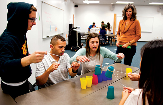 Students balancing colored cups with string on a desk