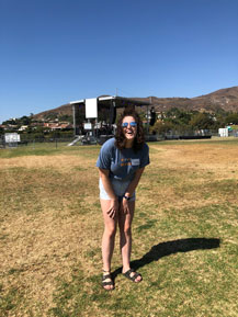 Tiffany Hall, slightly bent, smiling on Alumni Park in front of a stage