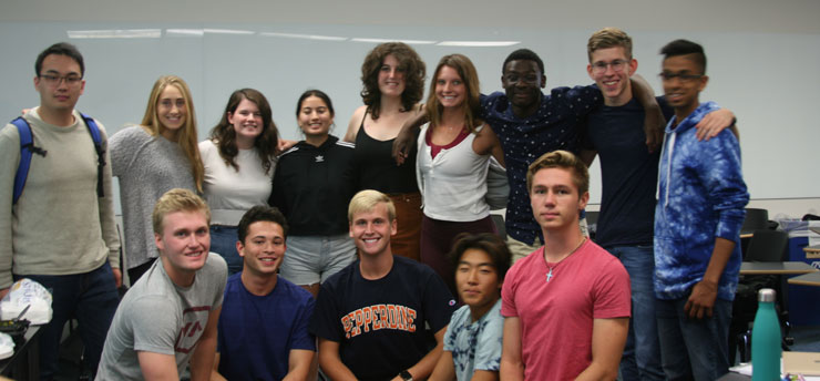 Debate team students gathered together in a classroom, pictured in front of a white board