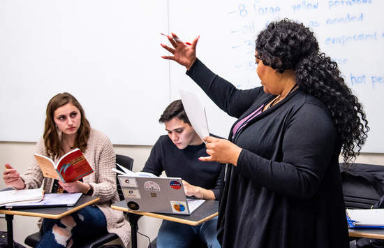 Professor with extended hand talking to students in her classroom