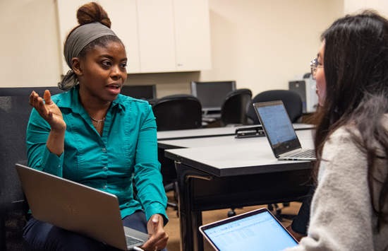 Dr. Joseph talking to a Seaver student, both are holding a laptop