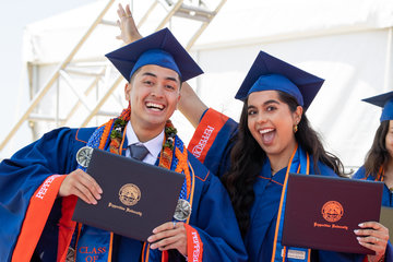 two students wearing caps and gowns holding diplomas