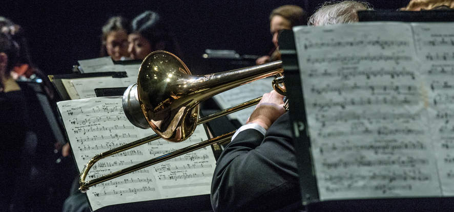 Orchestra students performing with sheet music and a trumpet taking center stage