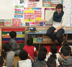 Student teacher pointing at a calendar to her students sitting on the floor