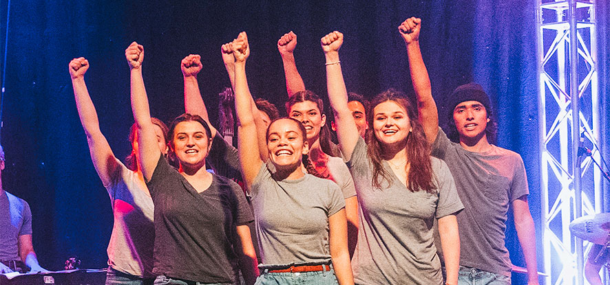 Students performing on stage with raised hands
