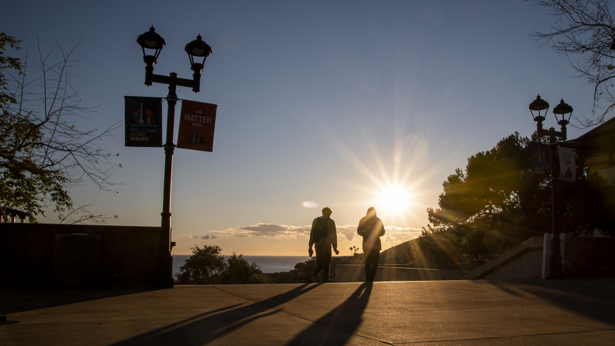 Two students walking into sunset on campus
